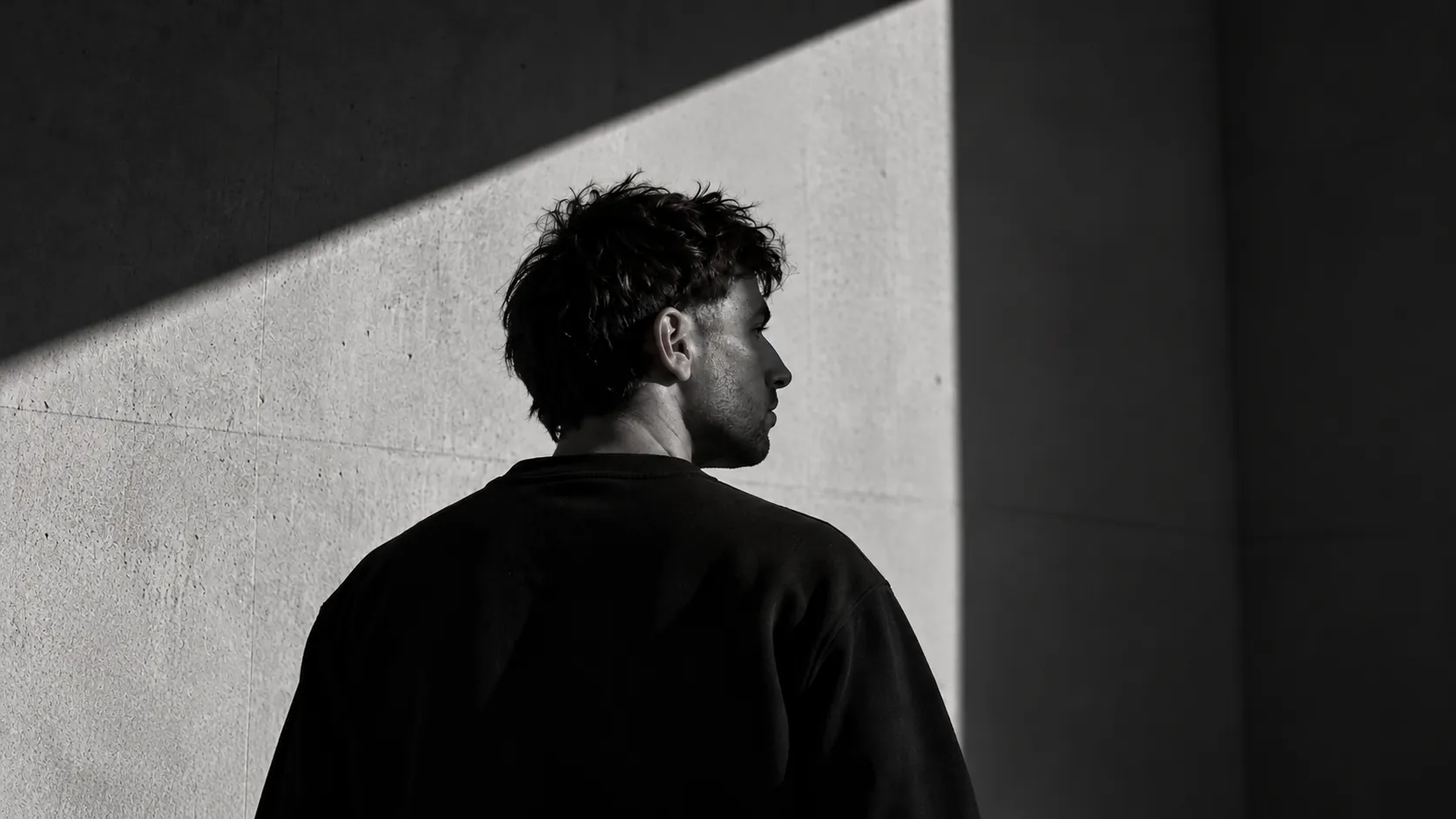 Clément Roux, de dos, devant un mur de béton éclairé en diagonale